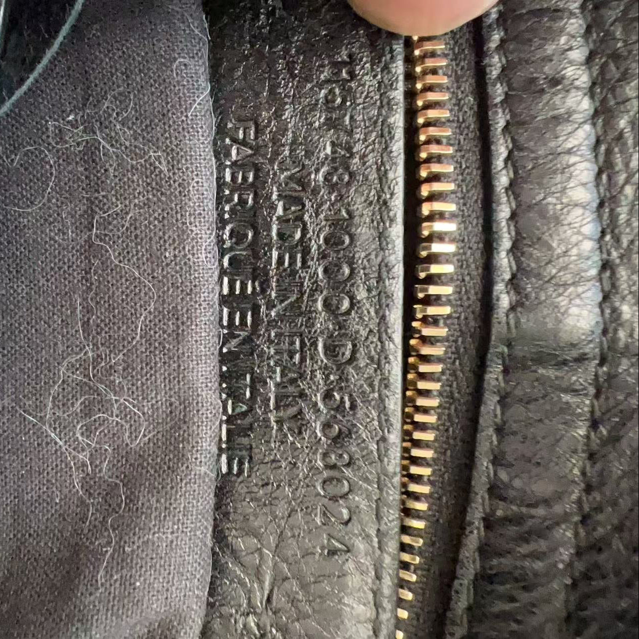Close-up of a dark gray leather zipper pull with embossed text reading 'HERMÈS PARIS' and a gray fabric lining with visible lint.
