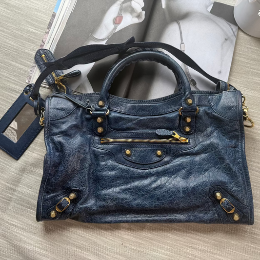 Blue handbag with gold accents on a light wooden surface