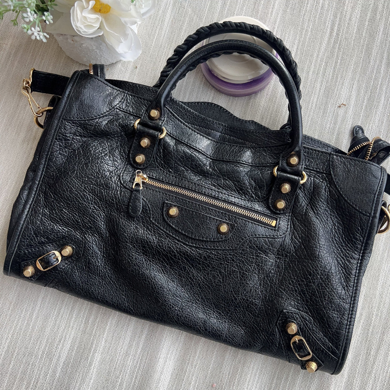 Black leather handbag with gold accents on a light wooden surface with flowers.