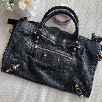 Black leather handbag with gold accents on a light wooden surface with flowers.
