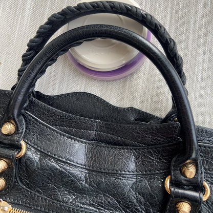 Black leather handbag with gold accents on a textured gray background