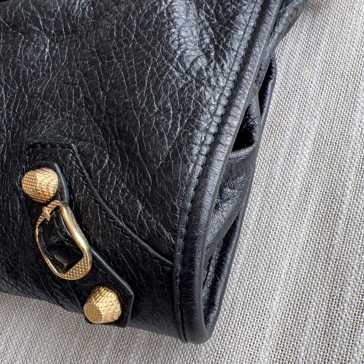Close-up of a black leather handbag with gold hardware on a gray fabric background
