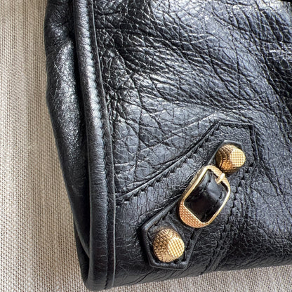 Close-up of a black leather handbag with gold hardware on a beige surface