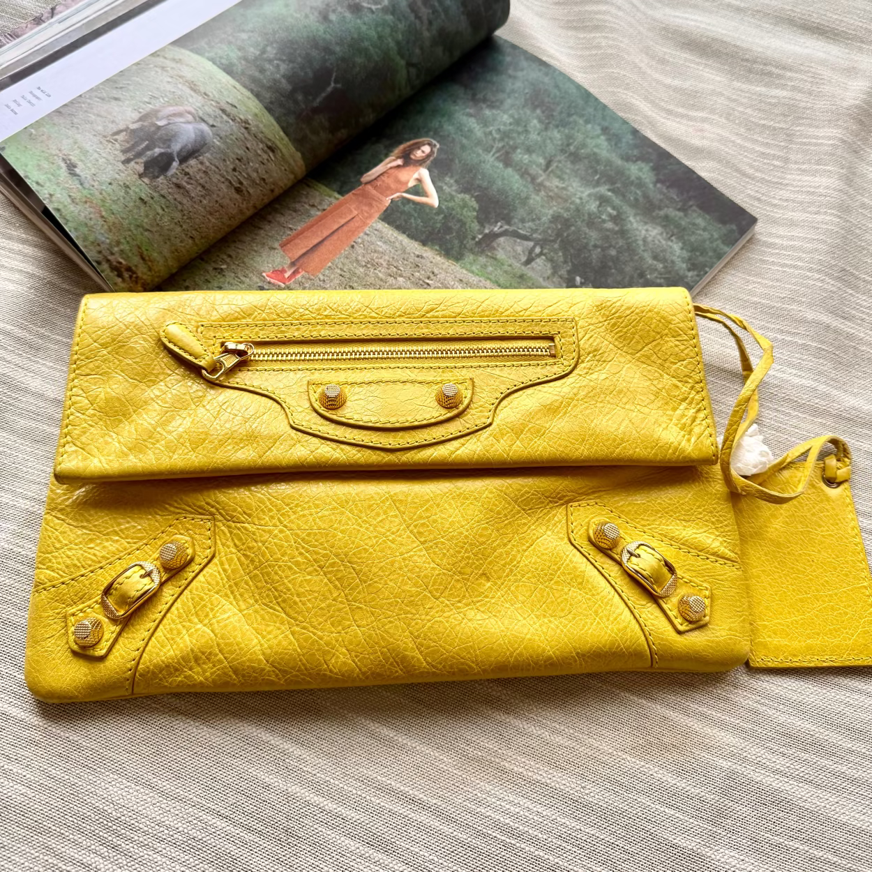 Yellow leather clutch bag on a wooden surface with an open magazine in the background