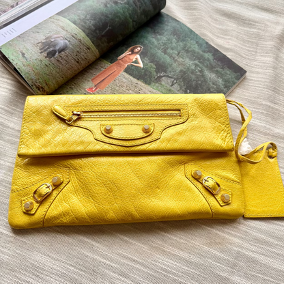 Yellow leather clutch bag on a wooden surface with an open magazine in the background