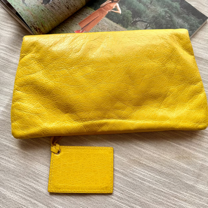 Yellow clutch bag on a textured surface with an open magazine in the background