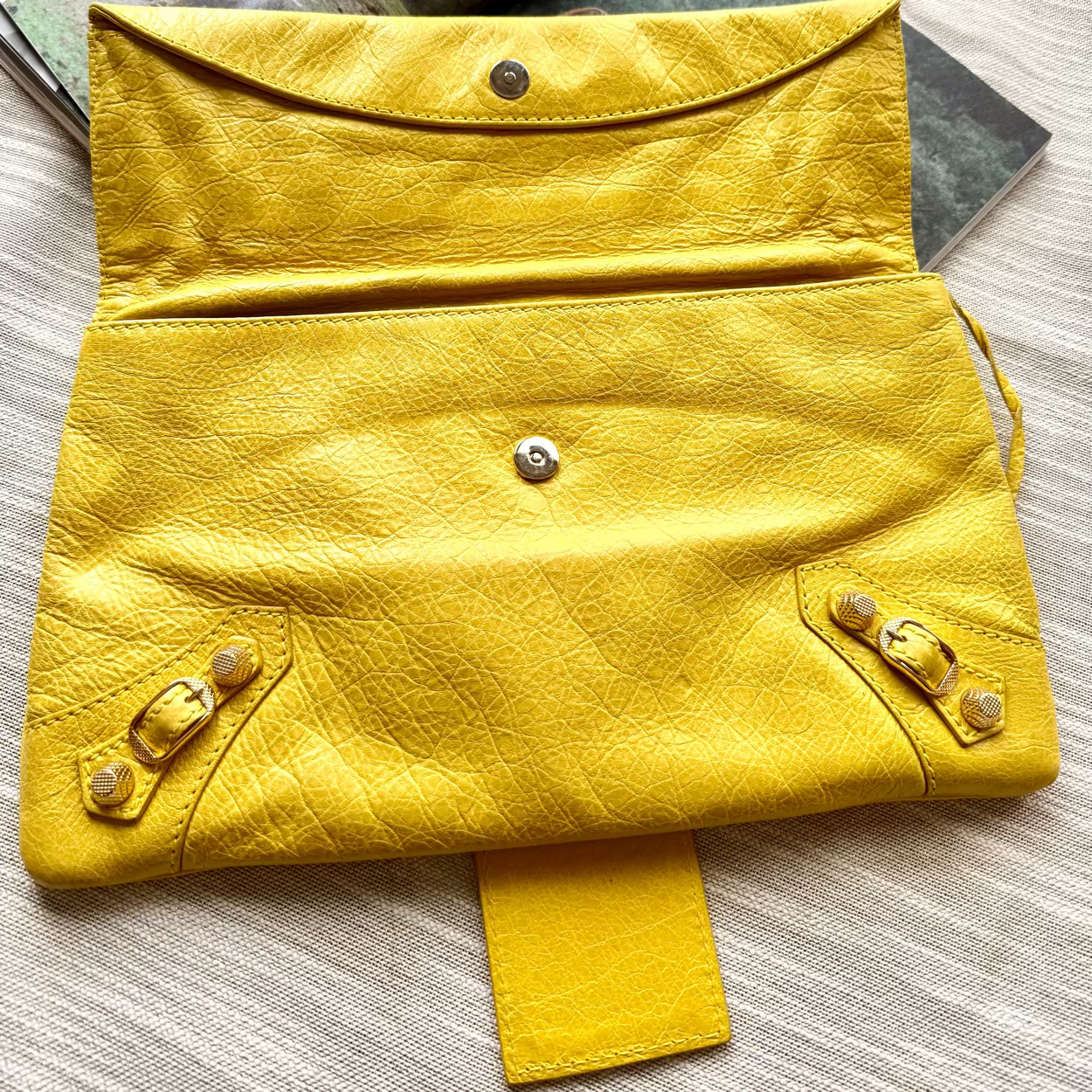 Yellow leather clutch bag on a textured surface with magazines underneath