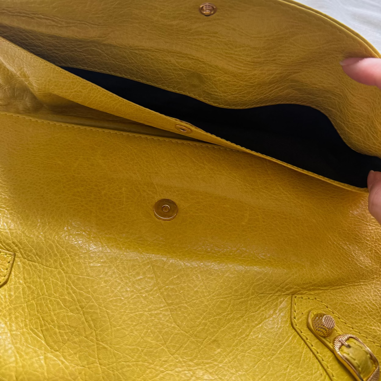 Yellow leather handbag with a person's hand opening it, on a light-colored surface.