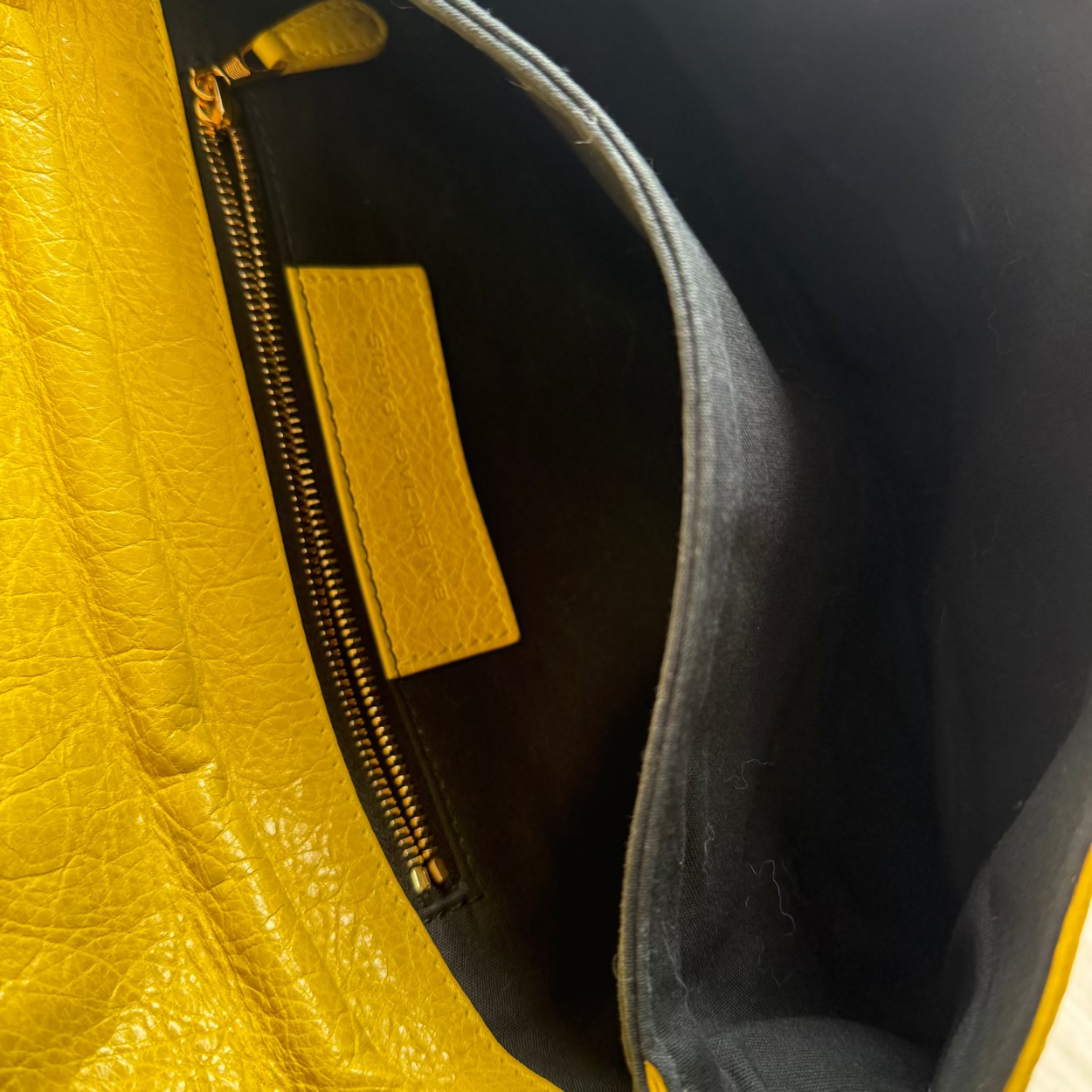 Close-up of a yellow leather handbag with a gold zipper and brand logo.