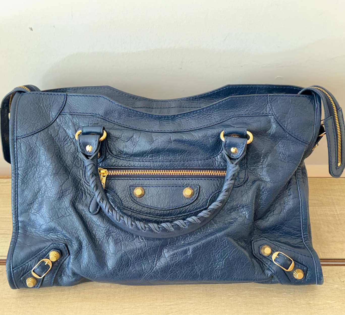 Blue leather handbag with gold hardware on a wooden surface