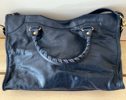 Black leather handbag with braided handle on a wooden surface