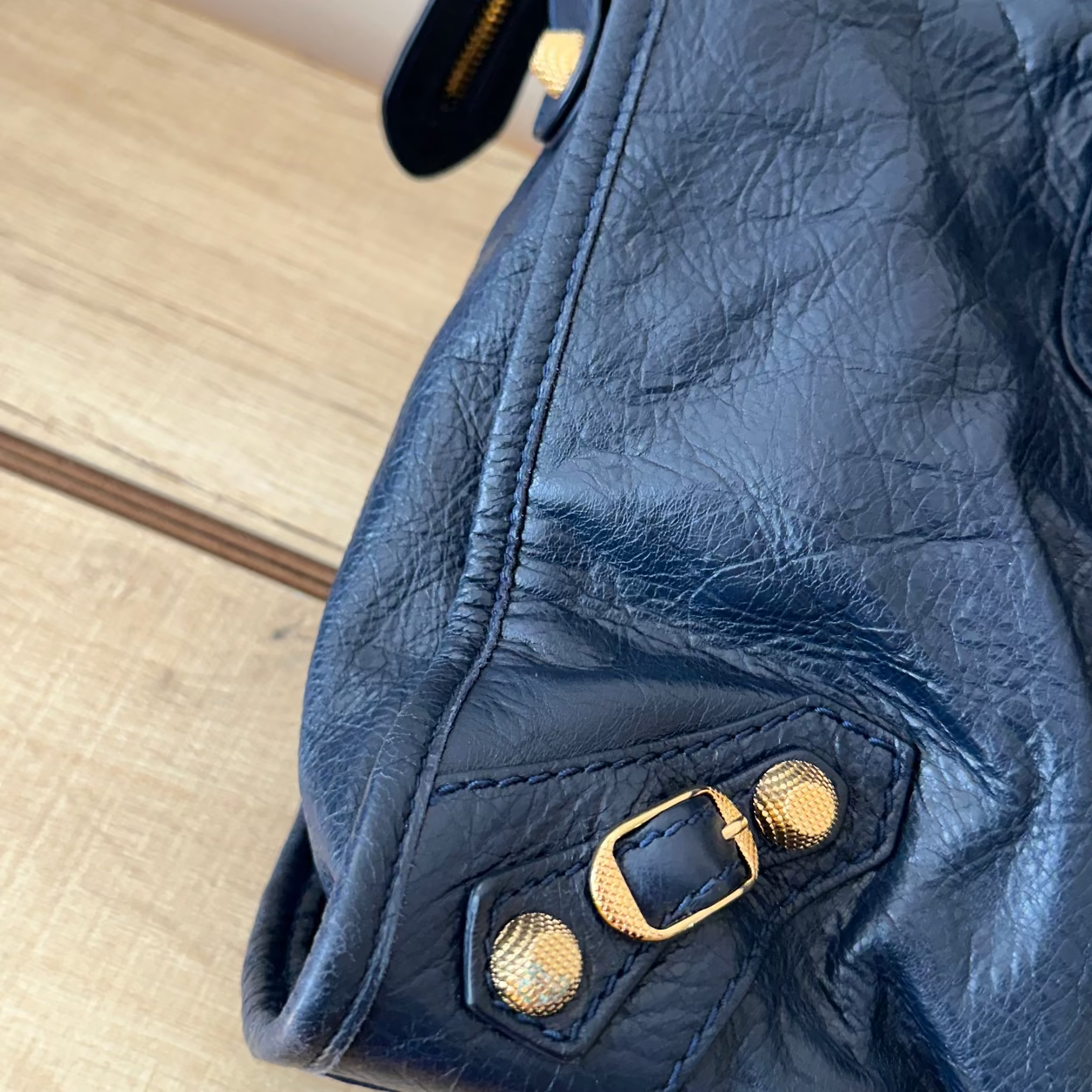 Close-up of a blue leather jacket with gold buttons on a wooden surface