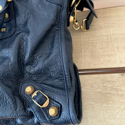 Blue leather handbag with gold hardware on a wooden surface