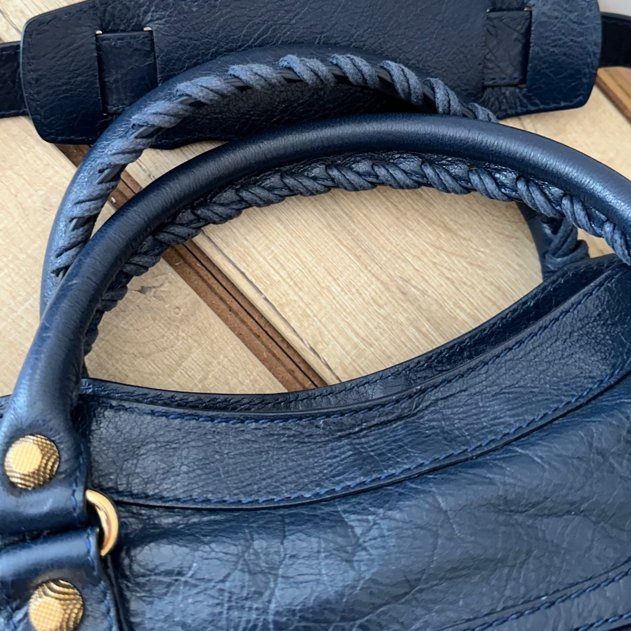 Close-up of a blue leather handbag with braided handle on a wooden surface