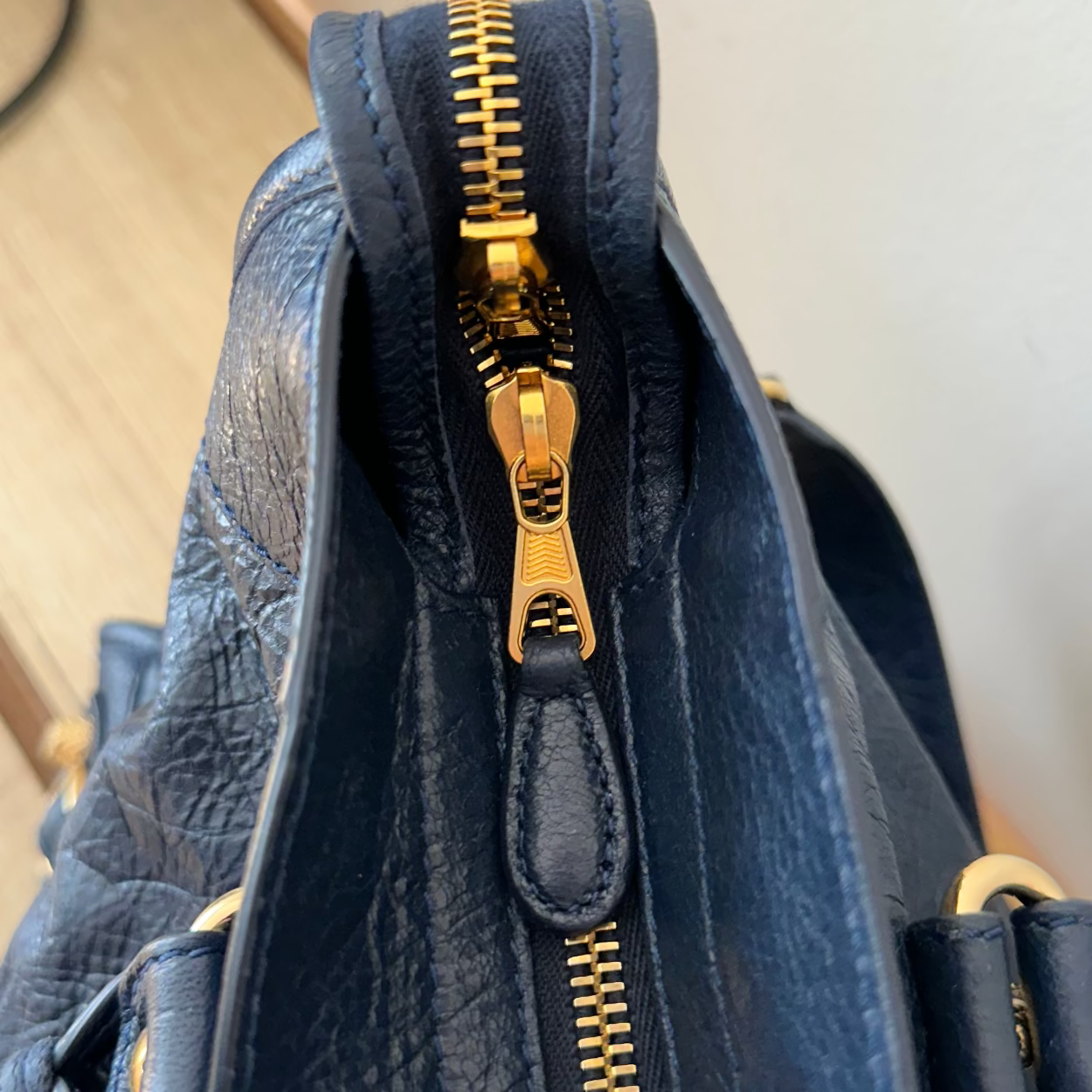 Close-up of a blue textured bag with a gold zipper on a neutral background