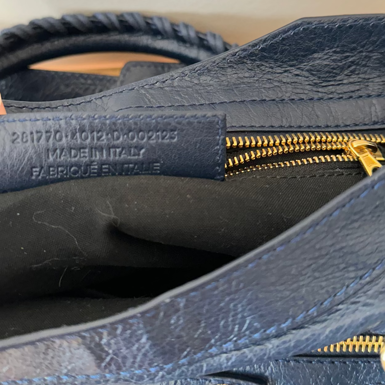 Close-up of a blue leather bag with gold zipper and visible 'Made in Italy' label.
