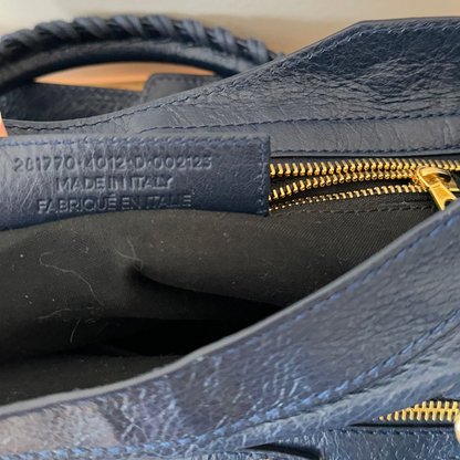 Close-up of a blue leather bag with gold zipper and visible 'Made in Italy' label.