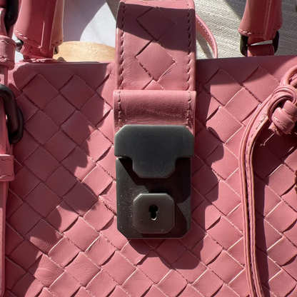 Close-up of a pink woven handbag with a visible lock mechanism.