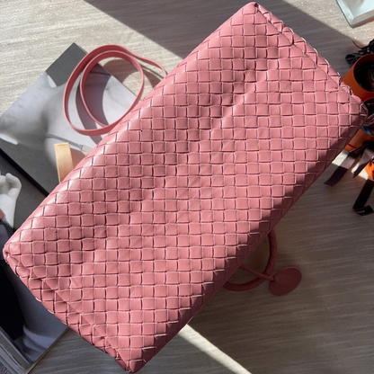 Pink woven clutch bag on a light wooden surface
