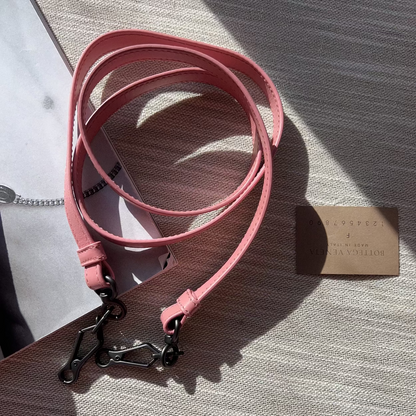 Pink leather dog leash with a metal clip on a textured surface