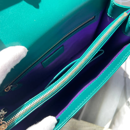 Close-up of a teal handbag with a gold zipper, held by a white gloved hand.