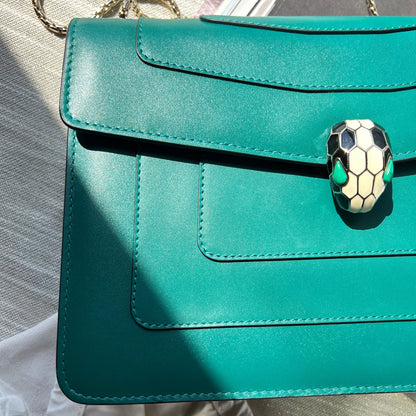 Teal handbag with a decorative clasp on a reflective surface