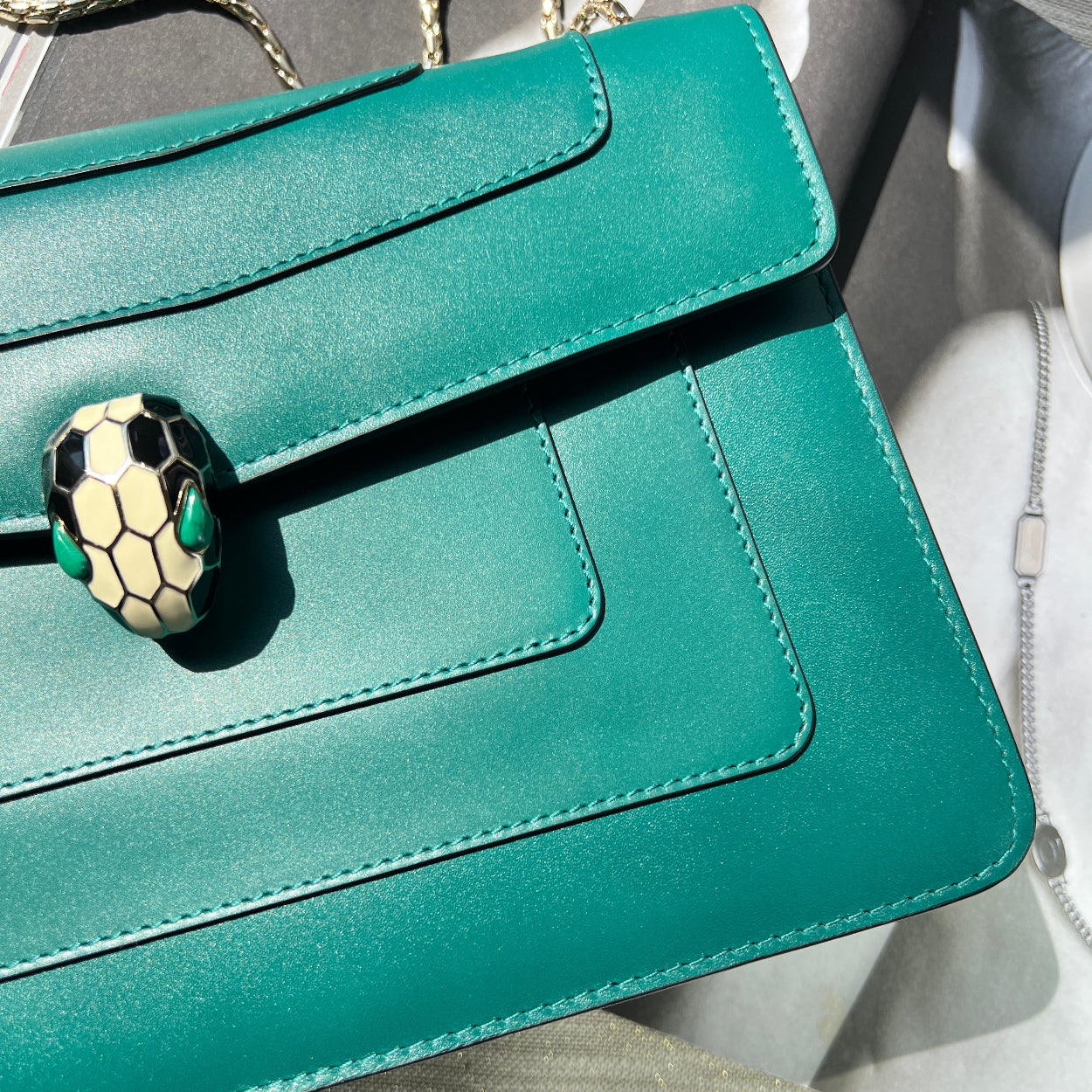 Teal handbag with a decorative clasp on a neutral background