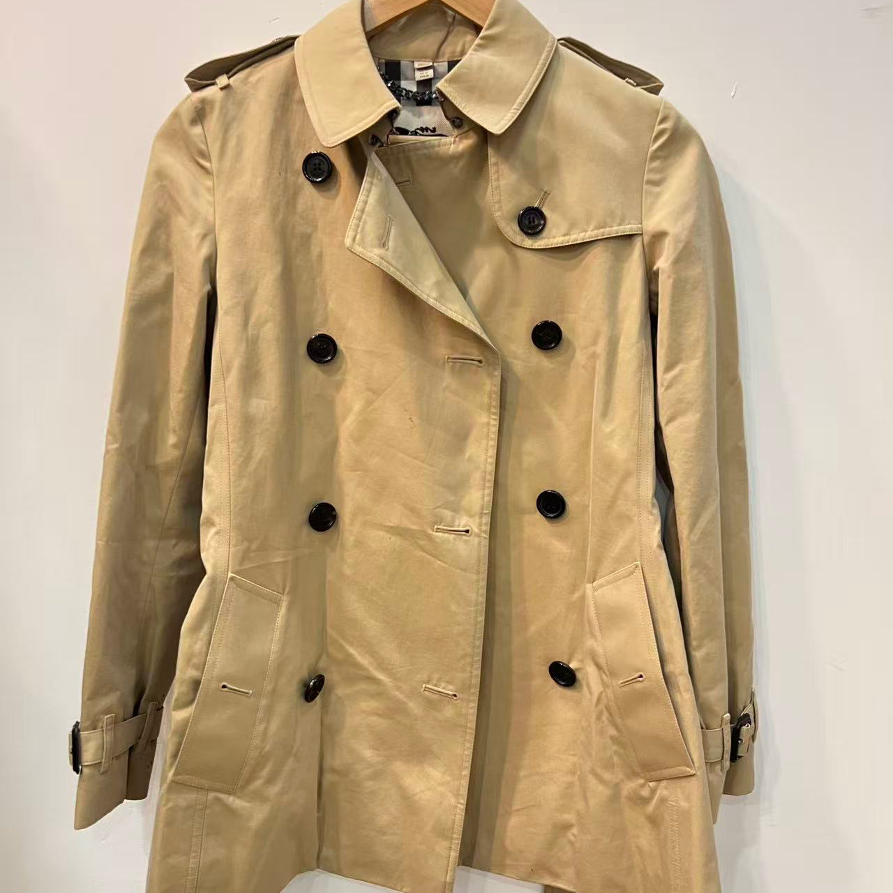 Beige trench coat on a hanger against a white background