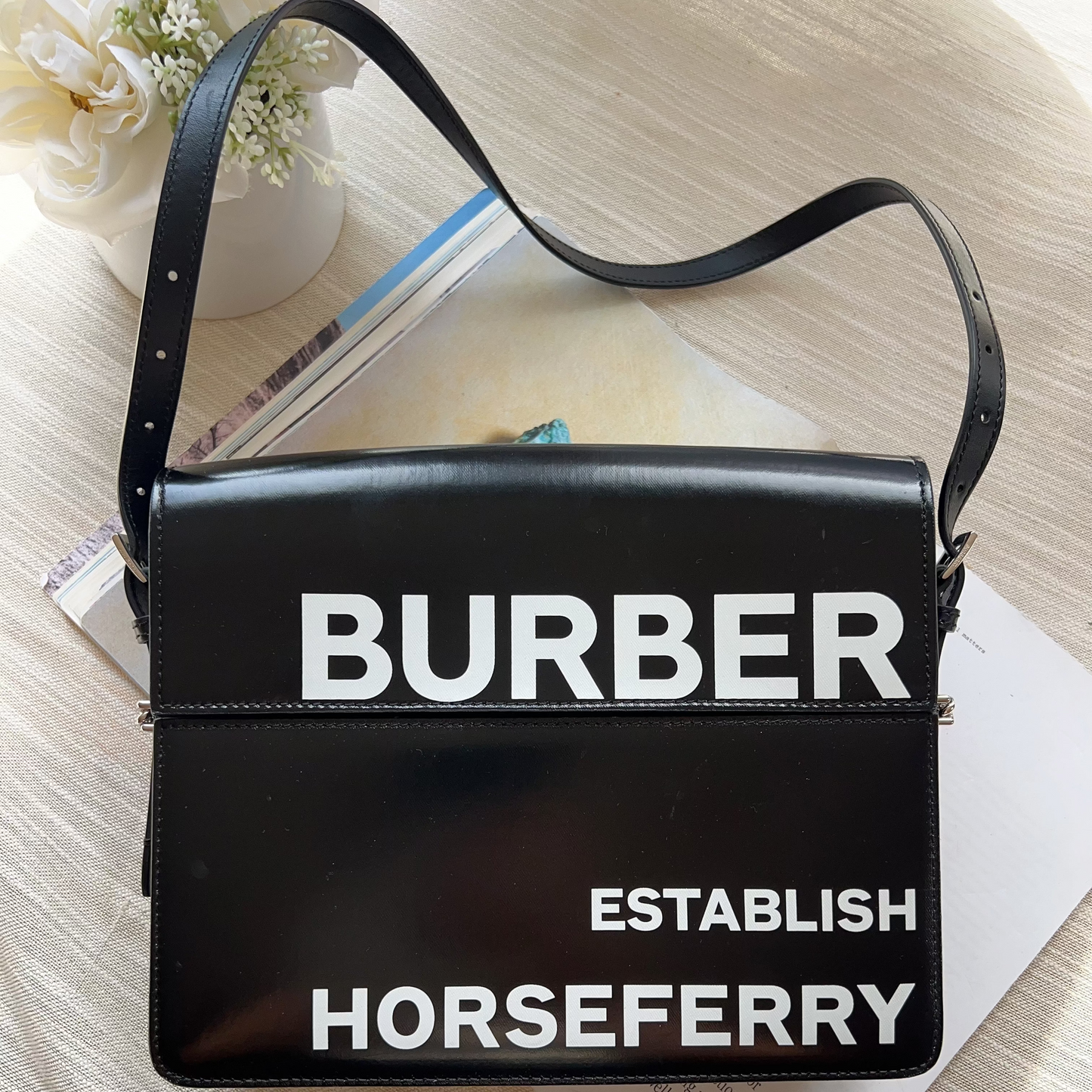 Black handbag with 'BURBER' and 'HORSEFERRY' text on a light wooden surface.