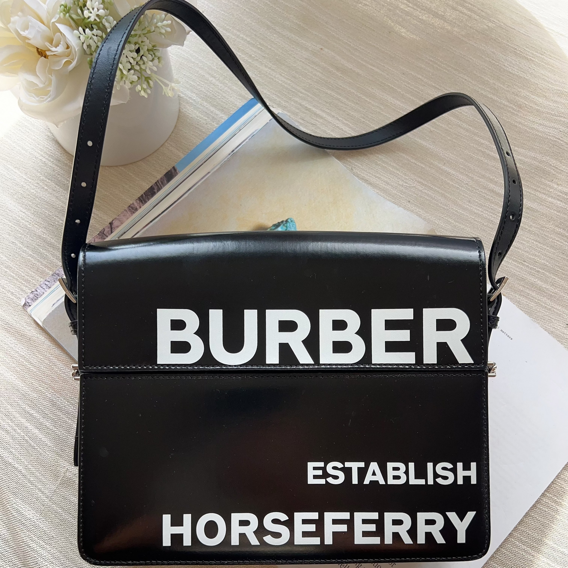 Black handbag with 'BURBER' and 'HORSEFERRY' text on a light wooden surface.