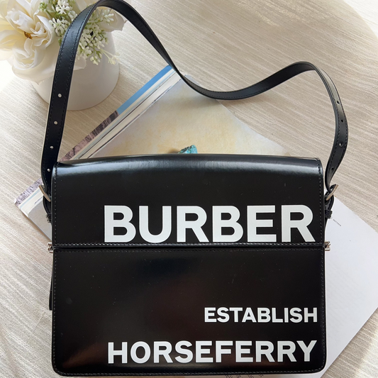 Black handbag with 'BURBER' and 'HORSEFERRY' text on a light wooden surface.