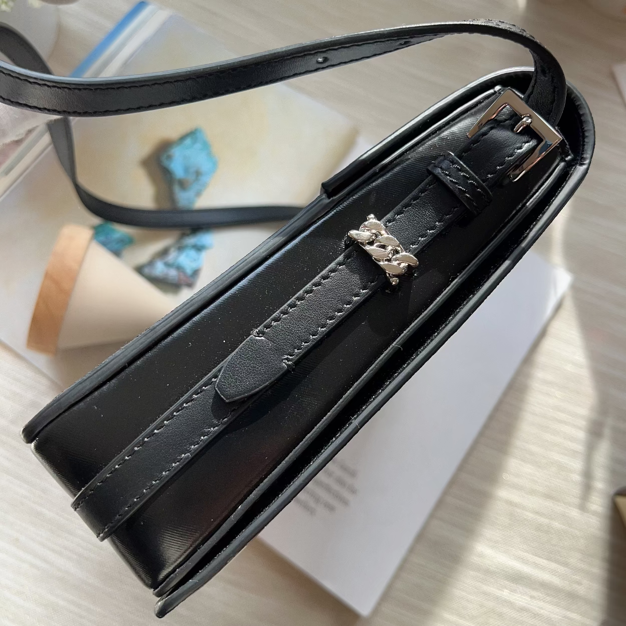 Black leather handbag with a decorative clasp on a light wooden surface.