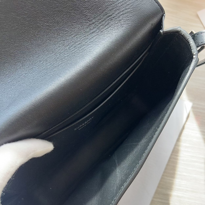 Close-up of a black leather handbag on a light wooden surface.