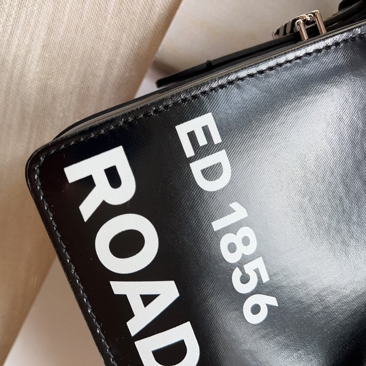 Black handbag with 'ED 1856 ROAD' text on a beige background