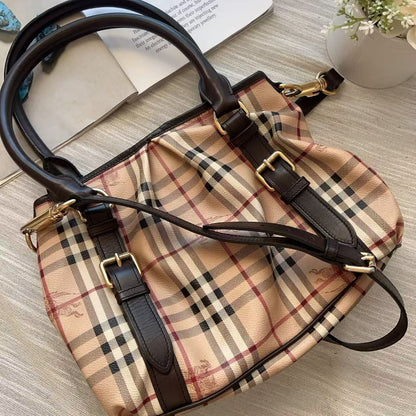 A classic Burberry-style plaid handbag in beige, black, and brown, featuring dark brown leather trim, double top handles, and gold-tone hardware, laid flat on a light wood-textured surface.