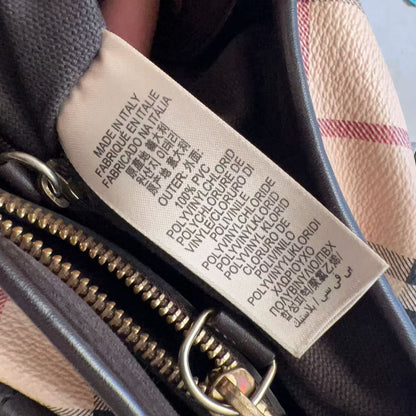 Close-up of a Burberry handbag interior showing a beige printed care tag with multilingual text, alongside dark brown leather trim and a beige plaid pattern.