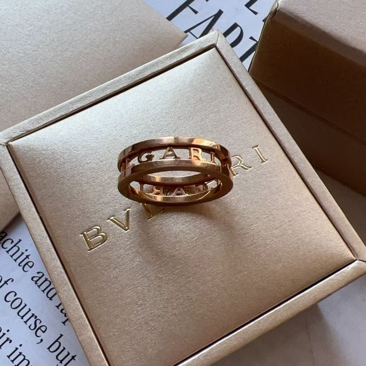 Two interlocking gold rings displayed on a beige Bvlgari box, with additional branded packaging visible around them.