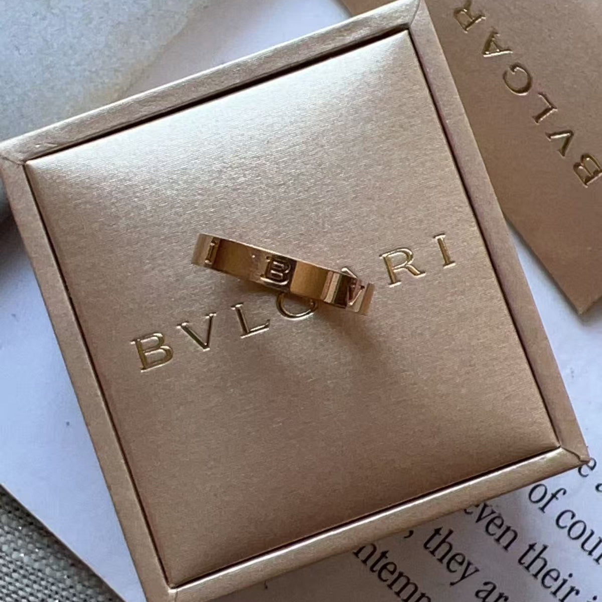 A gold-tone Bulgari ring displayed on a matching gold-tone jewelry box lid, with additional Bulgari packaging in the background.