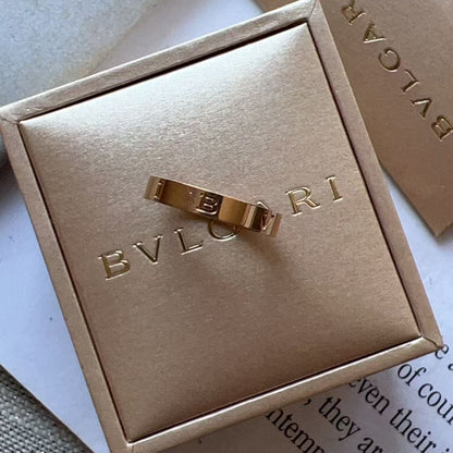 A gold-tone Bulgari ring displayed on a matching gold-tone jewelry box lid, with additional Bulgari packaging in the background.
