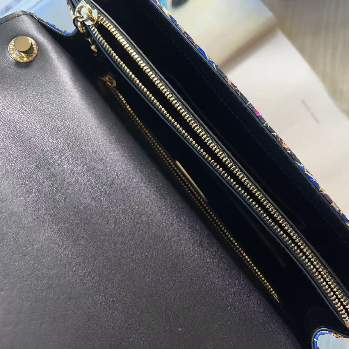 Close-up of a dark brown leather handbag interior showing gold-tone zippers, snap buttons, and a patterned fabric lining on the edge.