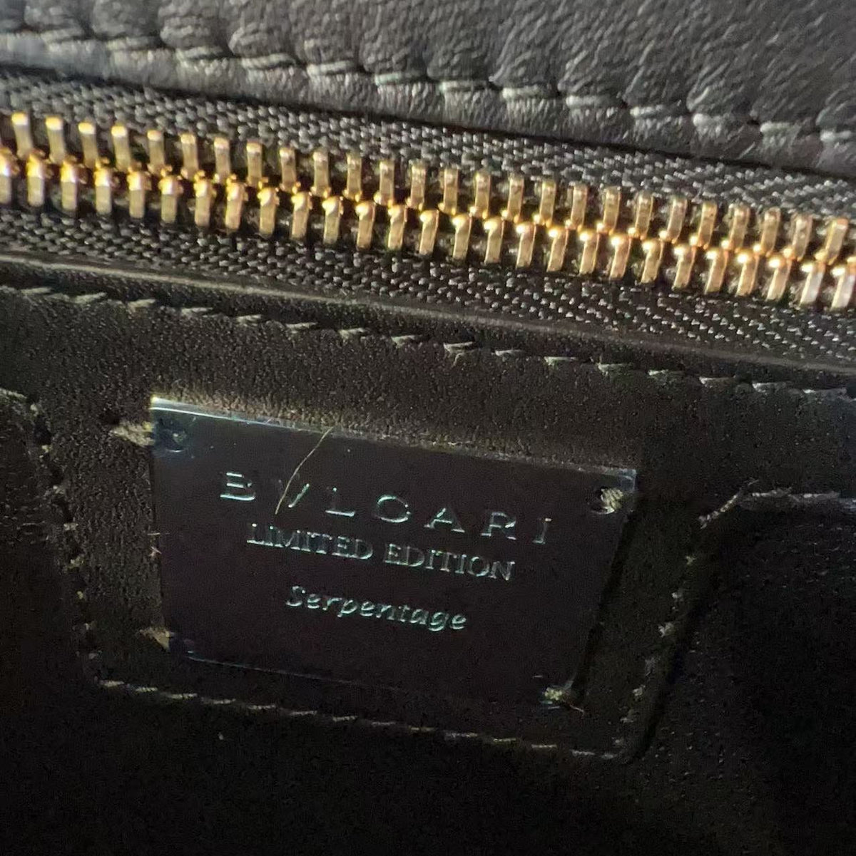 Close-up of a black leather Bvlgari Limited Edition Serpentine pouch with a gold zipper and a black metal brand plaque.