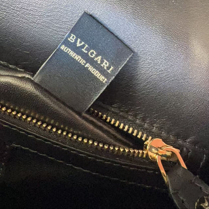 Close-up of a black leather zipper compartment with a black Bvlgari authentic product tag sewn inside, showing gold-tone zipper teeth and a small orange pull tab.