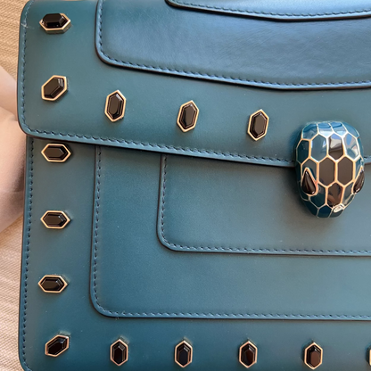Blue handbag with snake head clasp on a wooden surface