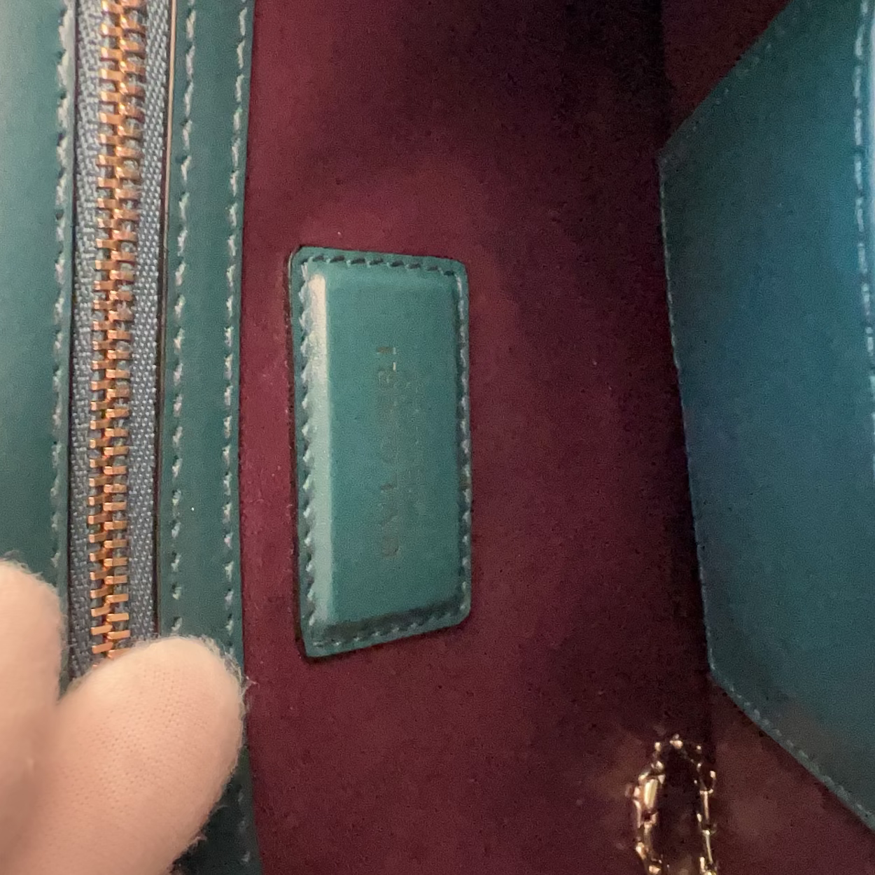 Close-up of a hand holding a maroon handbag with a visible brand label.