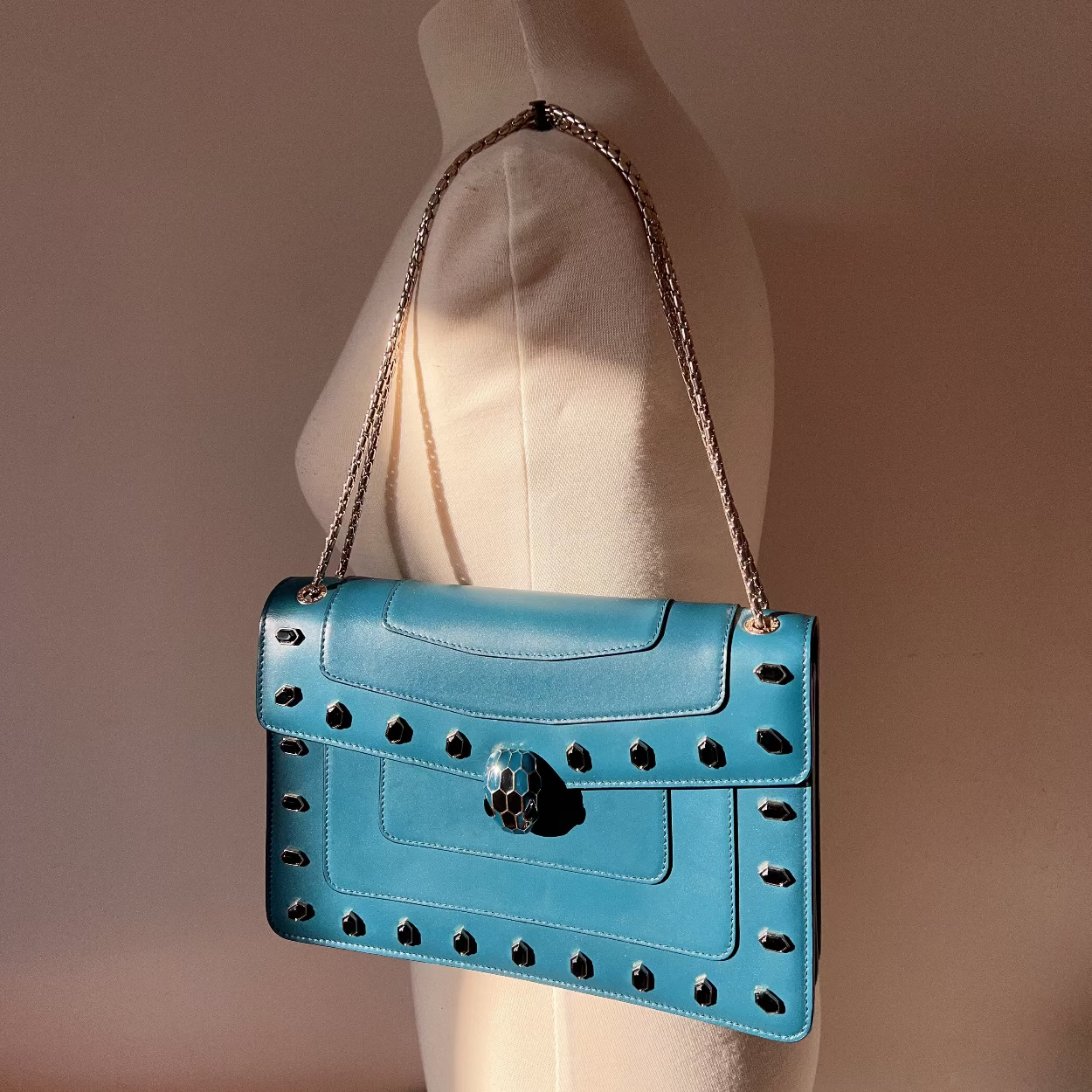 Blue handbag with cut-out design on a mannequin against a neutral background