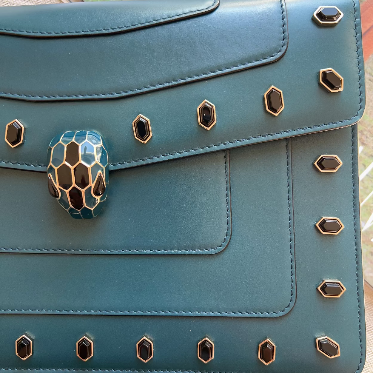 Teal handbag with snake head clasp on a wooden surface