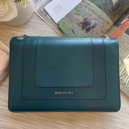 Green Bvlgari handbag on a wooden surface with a magazine in the background