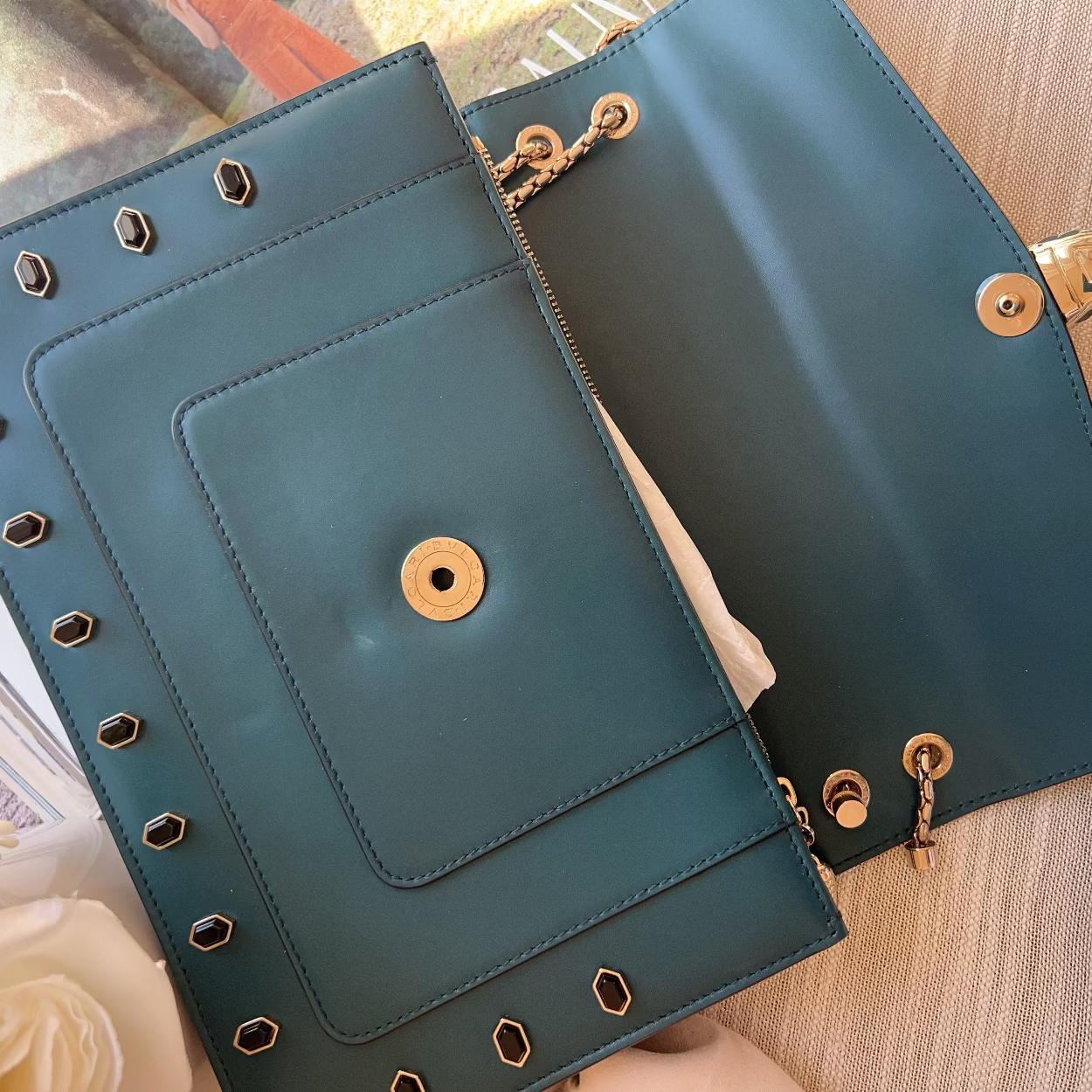 Two teal handbags with gold accents on a wooden surface.