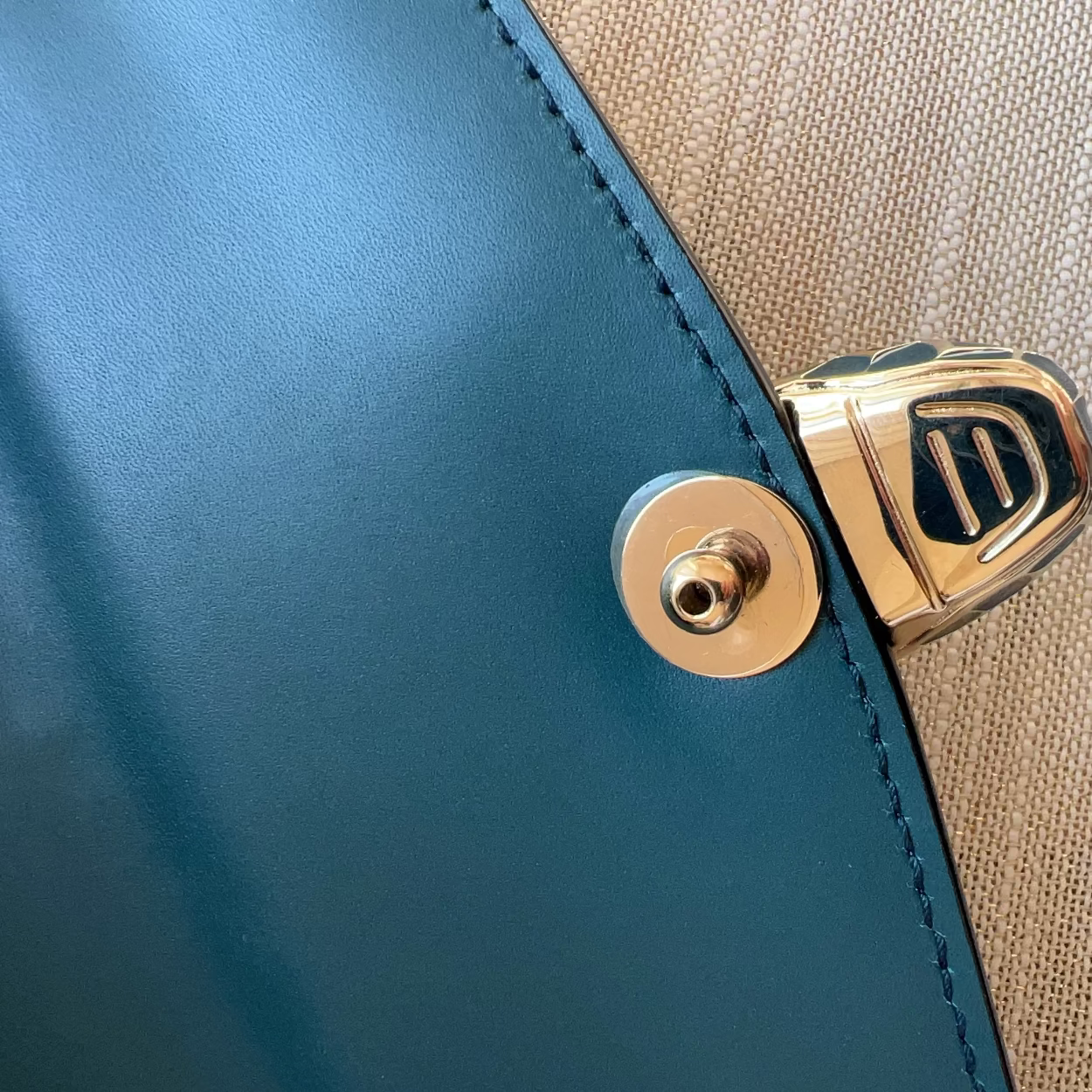 Close-up of a blue and beige leather product with a gold clasp.