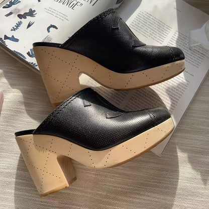 A pair of women's black pebbled leather mule clogs with chunky beige block heels, styled on a light fabric surface with an open magazine.